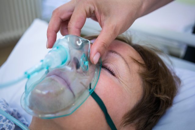 Uma enfermeira coloca uma máscara de oxigênio no rosto de um paciente de hospital.