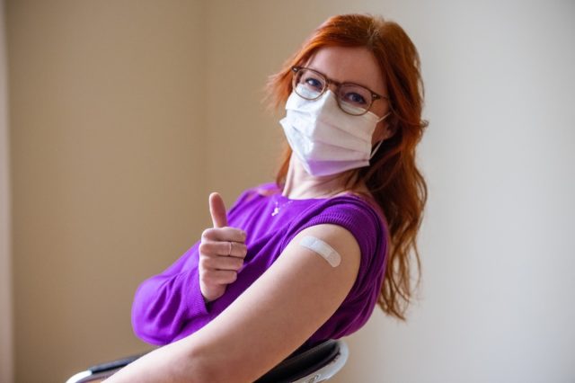 Uma mulher usando uma máscara facial olha para a câmera e mostra os polegares para cima depois de receber a vacina covid-19.