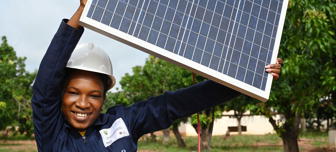 Na Costa do Marfim, uma adolescente segura um painel solar que está a estudar no âmbito de um curso de formação sobre energias renováveis.