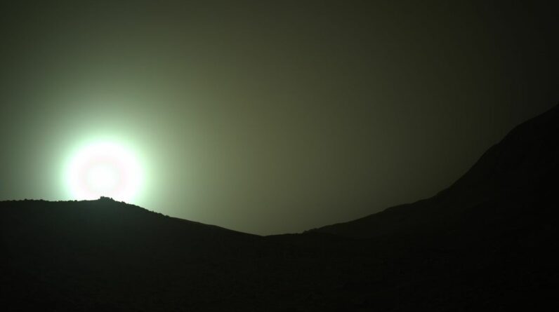 the sun rises through a red, dusty haze on mars