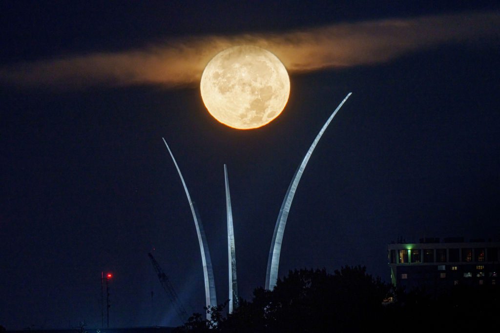 Uma lua cheia brilhante atrás de um punhado de nuvens acima de três grandes torres que se erguem no céu.