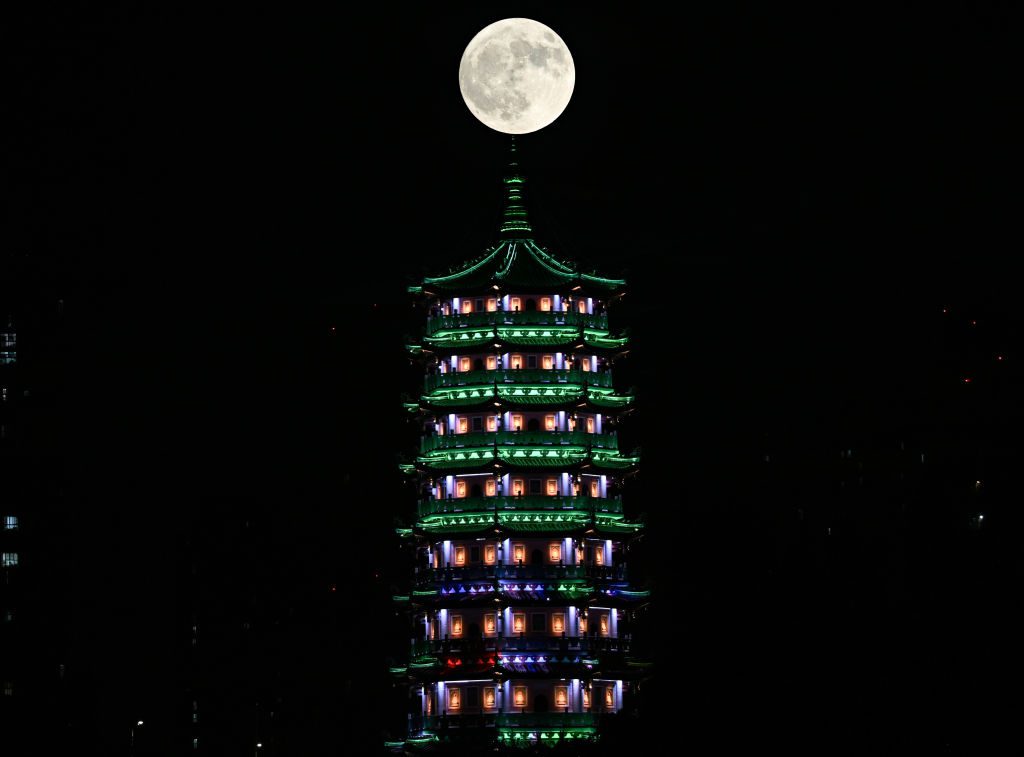 Uma estrutura alta de templo com uma lua grande e totalmente iluminada no topo.